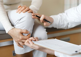 의료진이 무릎을 만져 보며 진료 기록을 작성하는 모습