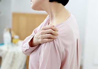 어깨 앞쪽을 손으로 짚으며 통증을 호소하는 모습