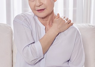 어깨를 감싸 쥐고 통증을 참고 있는 고령 환자