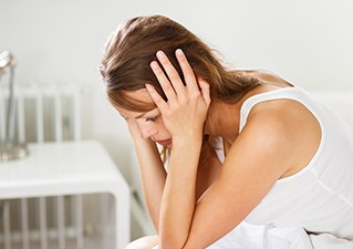 침대에 앉아 머리를 감싸 쥔 여성
